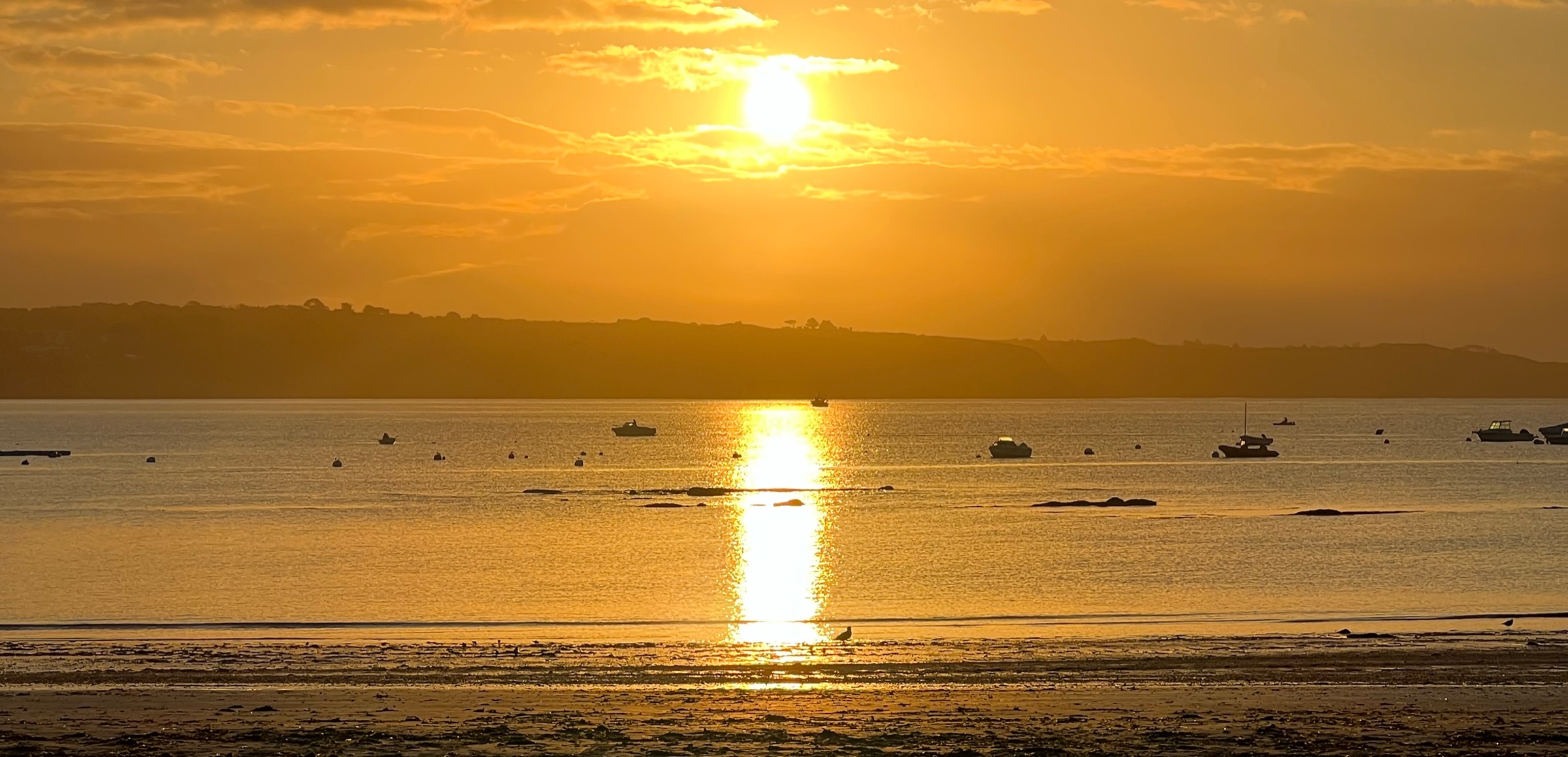La plage du Trez-Hir à Plougonvelin au coucher du soleil, bateaux au mouillage et reflet doré sur la mer.